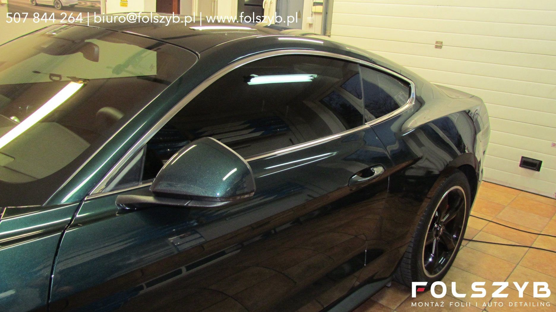 Ciemnozielony Ford Mustang w hali FOLSZYB po montażu folii na szybach bocznych, w szybie odbicie świetlówki