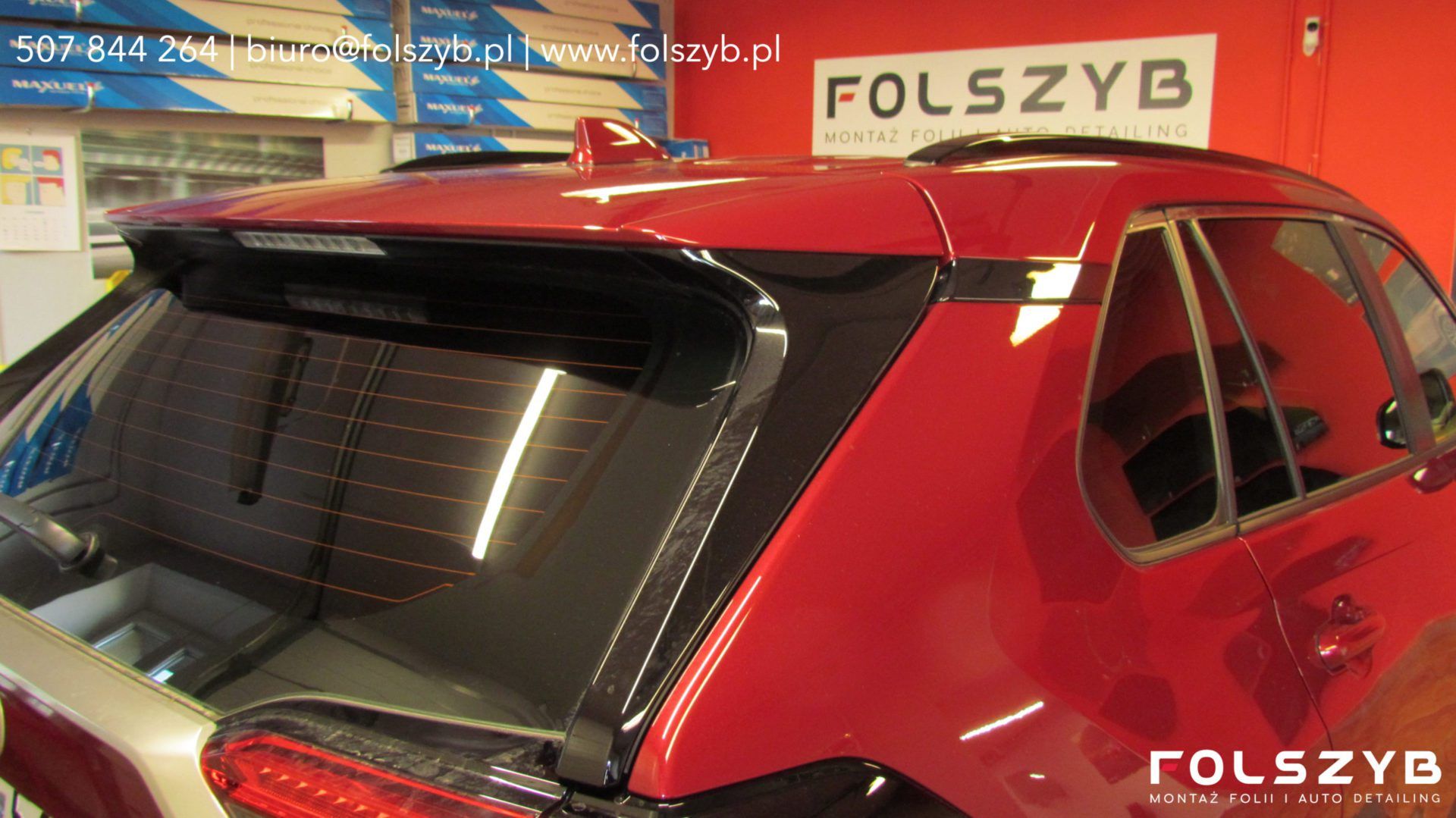 Tylna szyba czerwonej Toyoty RAV4 po montażu folii w hali FOLSZYB; przez folię widać ścieżki ogrzewania, na regale kartony z rolkami folii